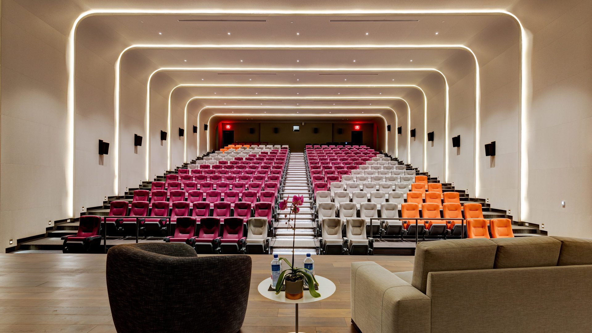 overview of large Hotel X Theatre with orange, purple and grey seats. at the front is a stage with sofa, chair and coffee table
