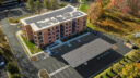 A complete aerial perspective showing the building, parking spaces with solar panel canopies and nearby natural greenery.