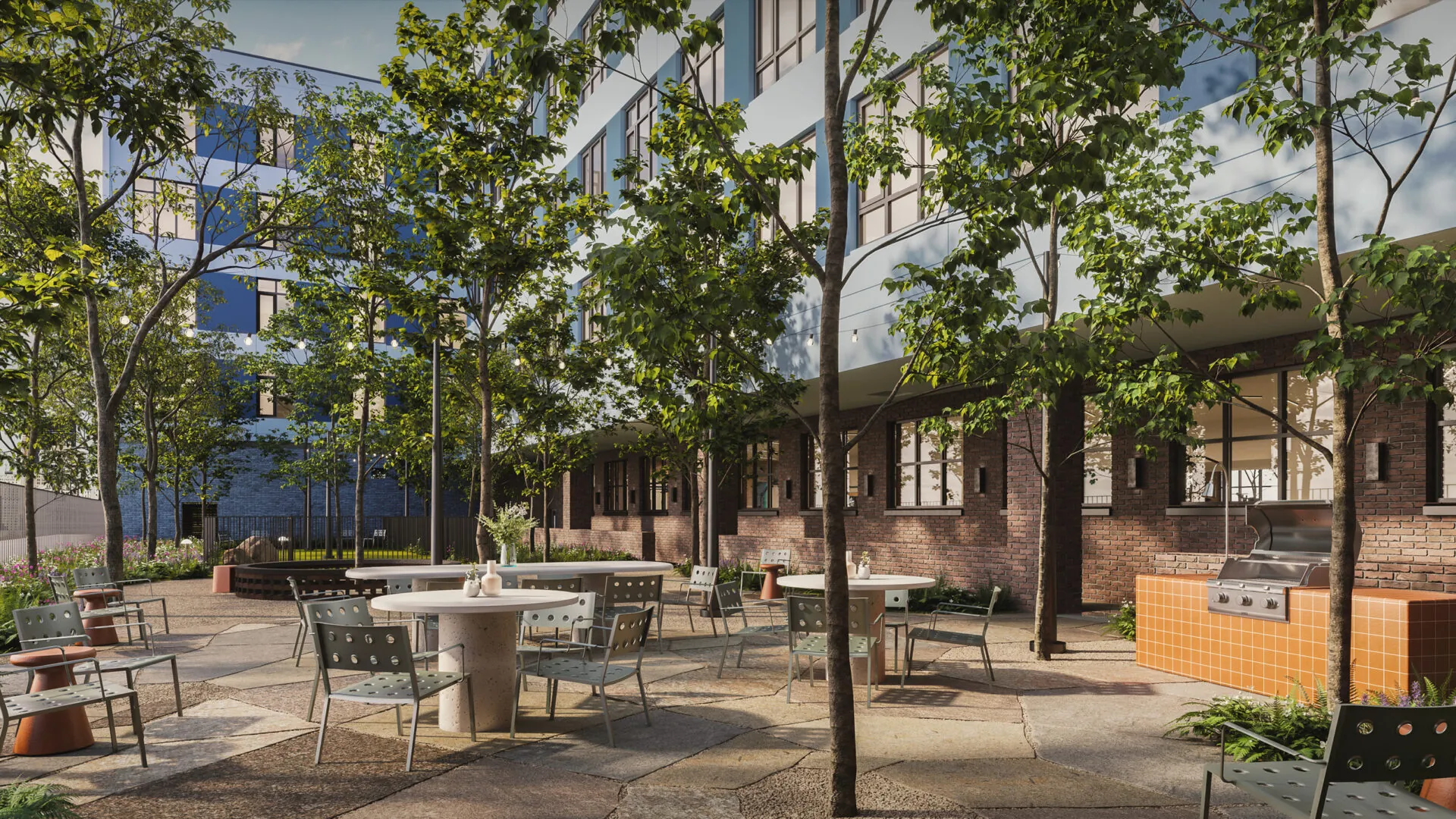 An outdoor patio area featuring tables and chairs surrounded by lush greenery. A barbecue station and trees provide a relaxing, inviting atmosphere.