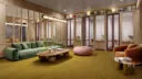 A lounge area with modern decor, featuring a green sofa, pink ottoman and wooden accents. The space is warm and inviting, with bookshelves and glass-paneled meeting rooms.