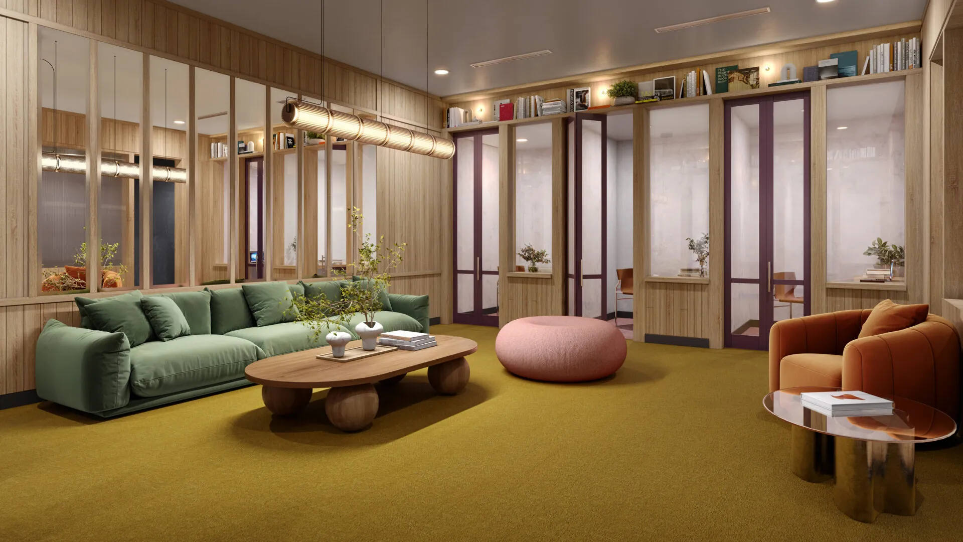 A lounge area with modern decor, featuring a green sofa, pink ottoman and wooden accents. The space is warm and inviting, with bookshelves and glass-paneled meeting rooms.