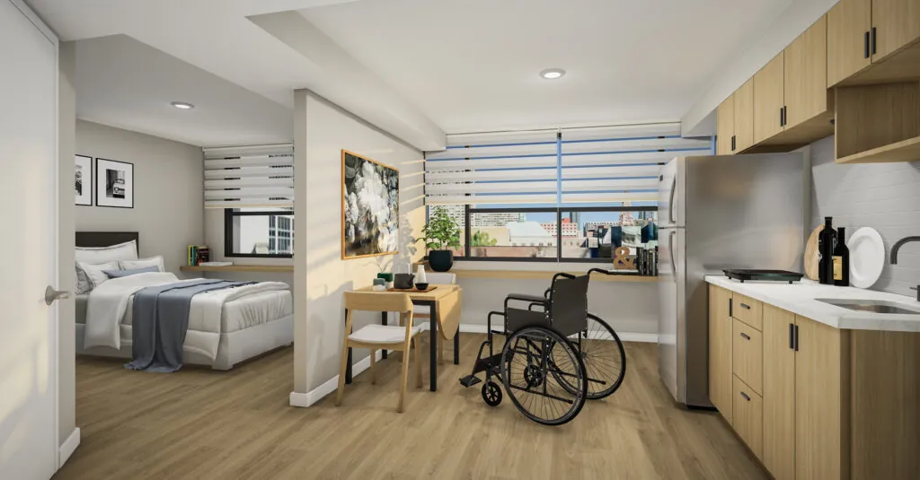 A modern, accessible studio apartment with a wheelchair features a combined living, dining, and kitchen area. The space includes a bed, a small dining table with a chair, a wheelchair, and a kitchen with wooden cabinets, a refrigerator, and a sink. Large windows with horizontal blinds allow natural light to fill the room. The decor is minimalistic with a few pieces of art and plants, creating a cozy and functional living environment.