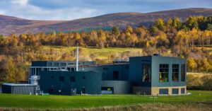Exterior view of whisky distillery against a backdrop of autumn trees and hills.