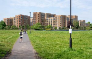 A paved straight path on a grassy field leading to a wide view of mid-rise student accommodation buildings.