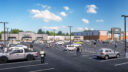 Spacious parking lot with scattered cars and people walking toward various retail stores under a partly cloudy sky.